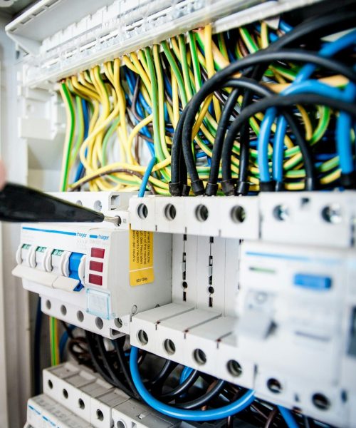 Hand of electrician working on a circuit breaker panel with colorful wires, ensuring safe electrical connections.